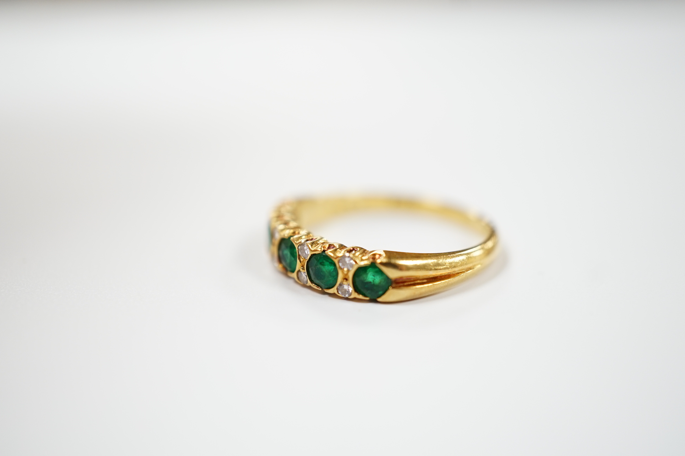 A modern 18ct gold and five stone emerald set half hoop ring, with diamond chip spacers, size K/L, gross weight 3 grams.